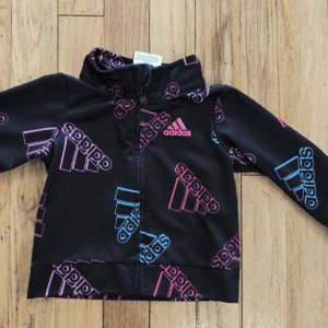 Black Adidas jacket with colorful logo patterns on wooden floor.