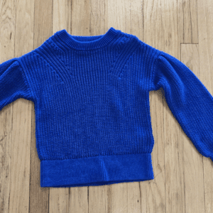 A blue knitted sweater laid flat on a wooden floor.