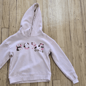Light pink hoodie with floral text design on the front, laid on wooden floor.
