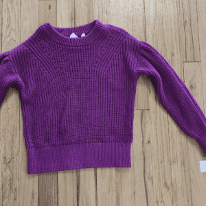 Purple knitted sweater laid on wooden floor.