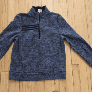 Blue quarter-zip sweater with black stripe detail, laid flat on wooden floor.