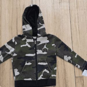 Children's camouflage hoodie with black sleeves and zipper, laid on wooden floor.