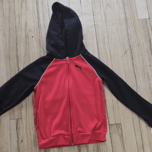 Red and black hooded jacket laid flat on a wooden floor.