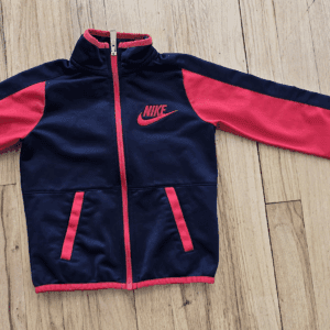 Nike jacket with navy blue and pink design laid on wooden floor.