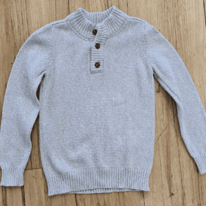 Light gray knitted sweater with buttoned collar laid flat on wood.