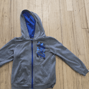 Gray hoodie with blue interior and zipper, laid flat on wooden floor.