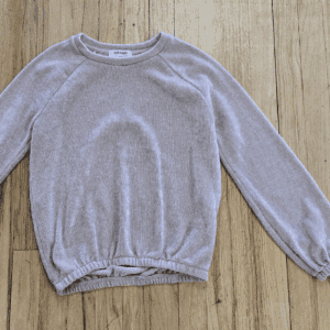 Light gray long-sleeve sweater on wooden floor.