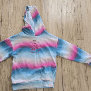 Colorful tie-dye hoodie laid flat on wooden floor.