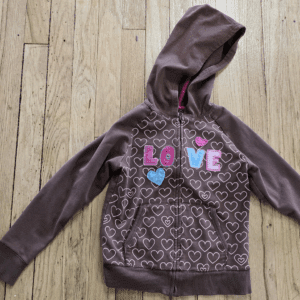 Brown hoodie with pink and blue love-themed print on wooden floor.