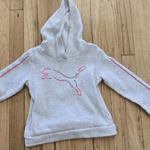 A gray Puma hoodie with pink accents laid on a wooden floor.