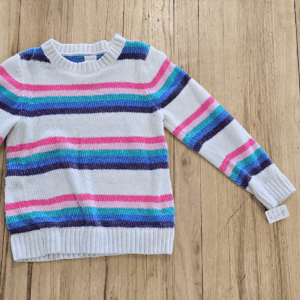 Colorful striped sweater laid flat on wooden floor.