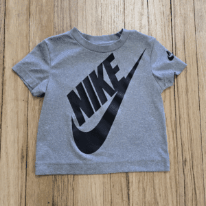 Gray Nike t-shirt with large black logo on wooden floor.