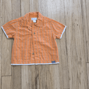Orange short-sleeve button-up shirt with white trim laid on wooden floor.