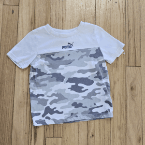 White and gray camouflage-patterned Puma t-shirt on wooden floor.