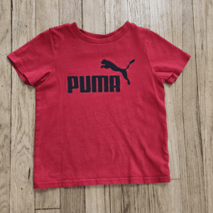 Red Puma T-shirt with black logo on wooden floor.