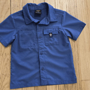 Blue short-sleeve button-up shirt with pockets, laid flat on a wooden surface.