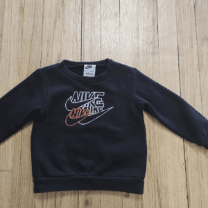Black Nike sweatshirt with multiple swoosh logos on a wooden floor.