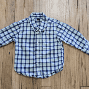 A blue and white plaid long-sleeve shirt laid flat on a wooden surface.