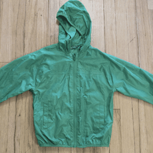 Green hooded windbreaker jacket laid flat on wooden floor.